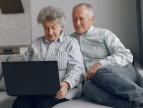 dwie starsze osoby siedzące na kanapie z laptopem w rękach 