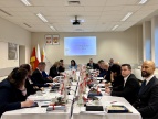 Sala konferencyjna podczas oficjalnego posiedzenia – przy długim stole siedzi kilkanaście osób w strojach formalnych, prowadzących obrady. Na stole leżą dokumenty, mikrofony, notatniki i filiżanki z kawą, a pośrodku ustawione są dekoracje świąteczne. Na ścianie wyświetlona jest prezentacja z tytułem „Uchwała budżetowa Gminy Dobczyce na 2026 rok”, obok wiszą godła i flagi. Uczestnicy skupieni są na dyskusji i notowaniu.