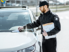 policjant wkładający manadat za szybę białego samochodu
