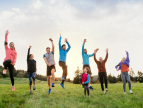 osoby w różnym wielku podskakują na trawie z rękami wyciągniętymi ku górze