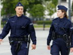 Dwoje policjantów w granatowych mundurach patroluje teren w przestrzeni miejskiej.
