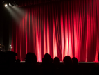 bordowe kotary na scenie na które pada oświetlenie, widać też publiczność siedzącą na trybunach