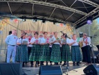 Grupa kobiet w tradycyjnych strojach ludowych występuje na scenie podczas wydarzenia plenerowego.
