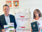burmistrz Tomasz Suś trzyma w dłoniach informatory dotyczące Nordic Walking, obok stoi Anna Opałek-Bassara trzyma dokument w granatowej teczce z logo gminy