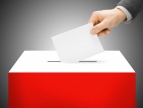 biało-czerwona urna, do której wkładany jest biały arkusz trzymany w dłoni