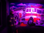 Duża ściana z namalowanym wozem strażackim i podświetlanym światłem na fioletowo.