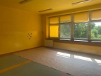 Duża przestrzenna sala z oknami. Sala ma kolor żółty