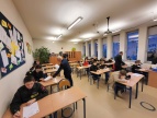 w sali lekcyjnej w ławkach siedzą uczestnicy turnieju, członkowie komisji rozdają uczestnikom testy